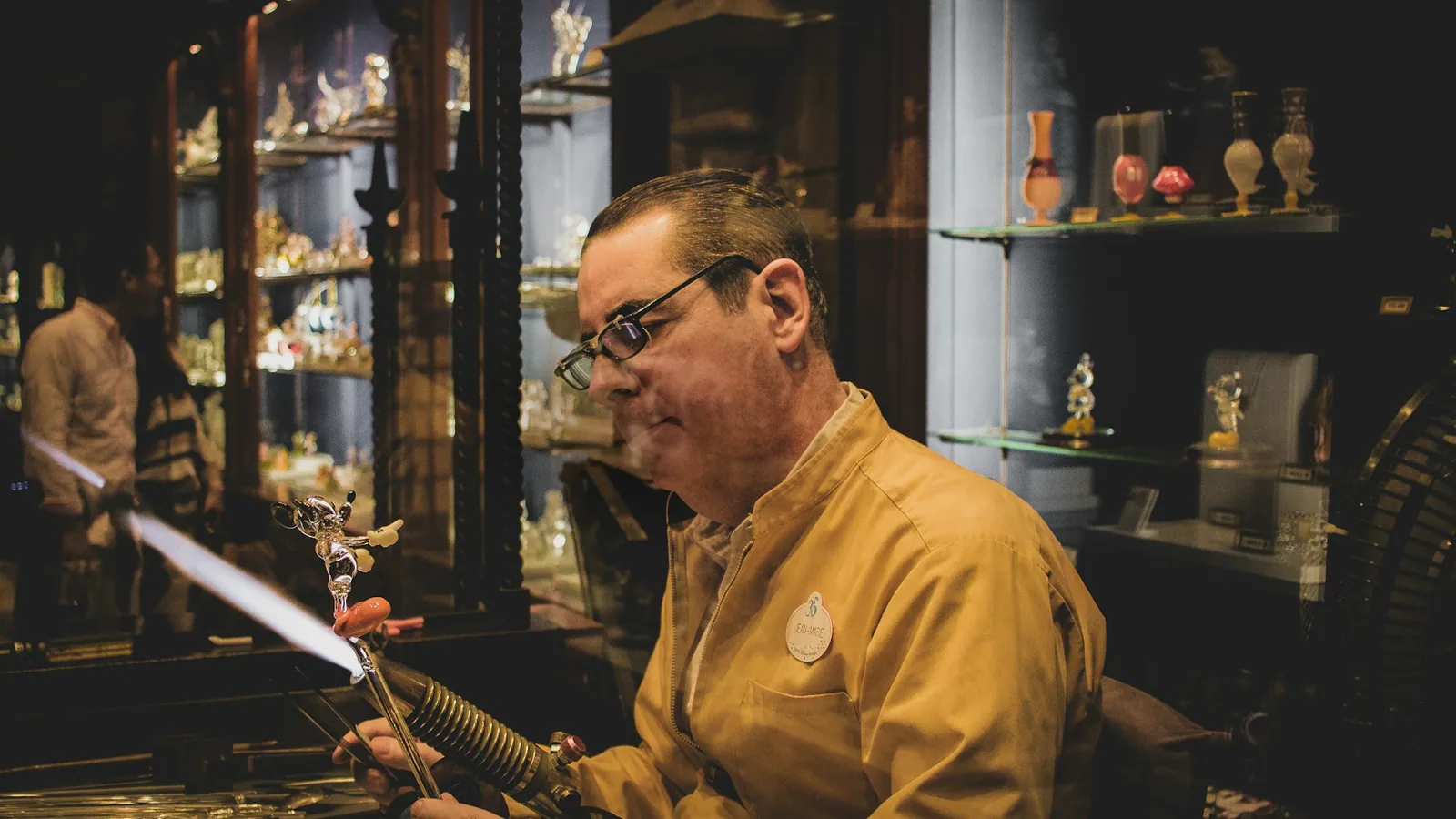 Client feuilletant un catalogue d'atelier avec des pièces d'artisan-créateur exposées, ambiance chaleureuse d'atelier-galerie.