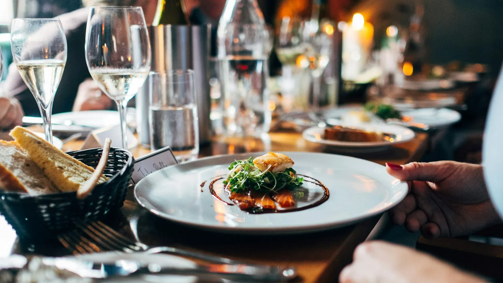 Table dressée d'un restaurant indépendant, lumière chaude, carafe et verres en premier plan, salle soignée en arrière-plan.